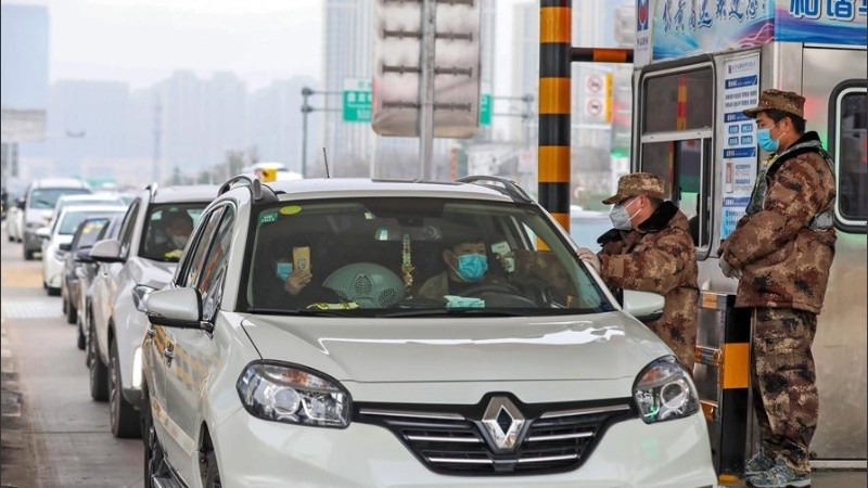 Un militar revisa la temperatura de un automovilista en un puesto de Wuhan.