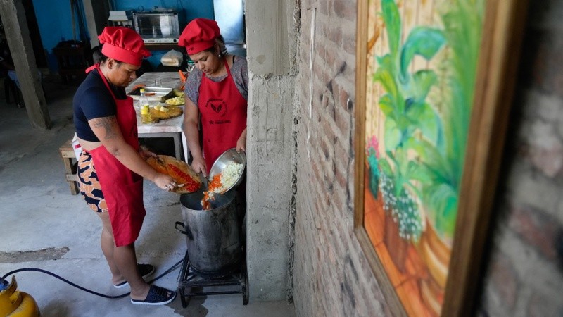 Las cocineras tirando las verduras cortadas en la olla para sumar al menú de arroz con pollo.